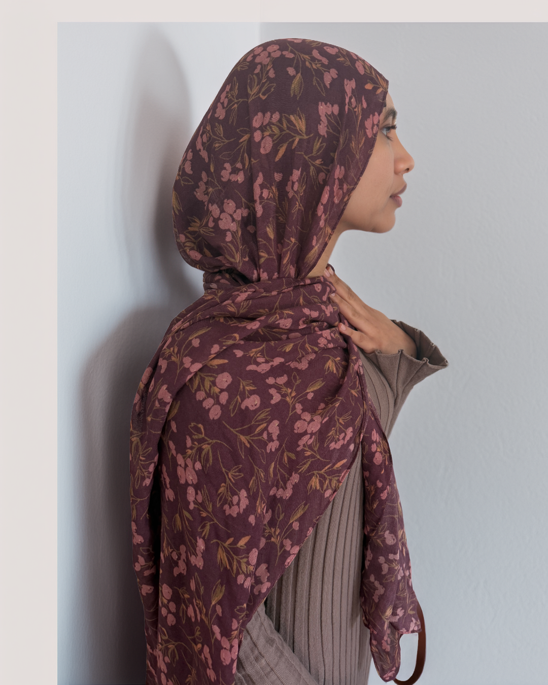 Woman wearing a dark floral hijab against a light background